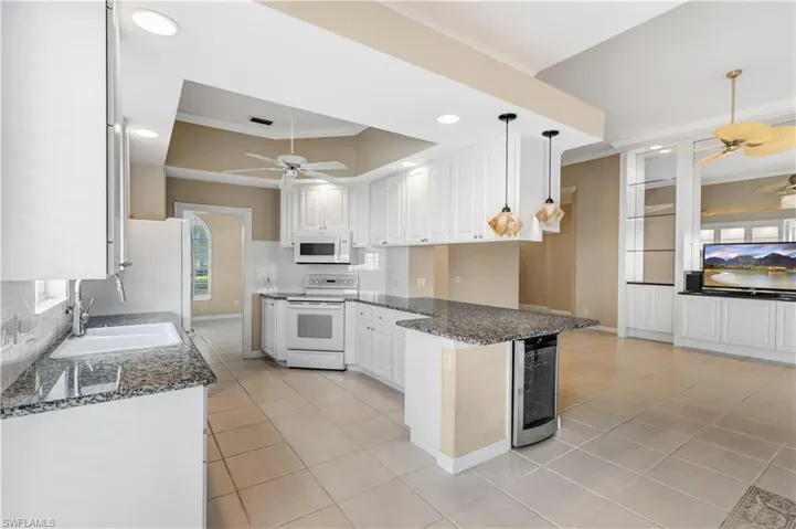 Kitchen featuring white appliances, ceiling fan, a sink, a raised ceiling, and wine cooler