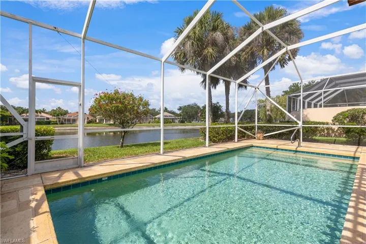 Swimming pool with glass enclosure, a water view, and a patio area