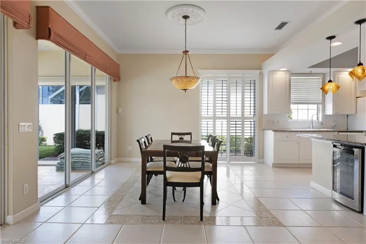 Dining space featuring wine cooler, light tile and plantation shutters,patterned flooring, ornamental molding, baseboards, and inlaid floor details