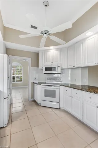 Kitchen with white appliances, white cabinets, ceiling fan, light tile patterned floors, and backsplash leading to Den