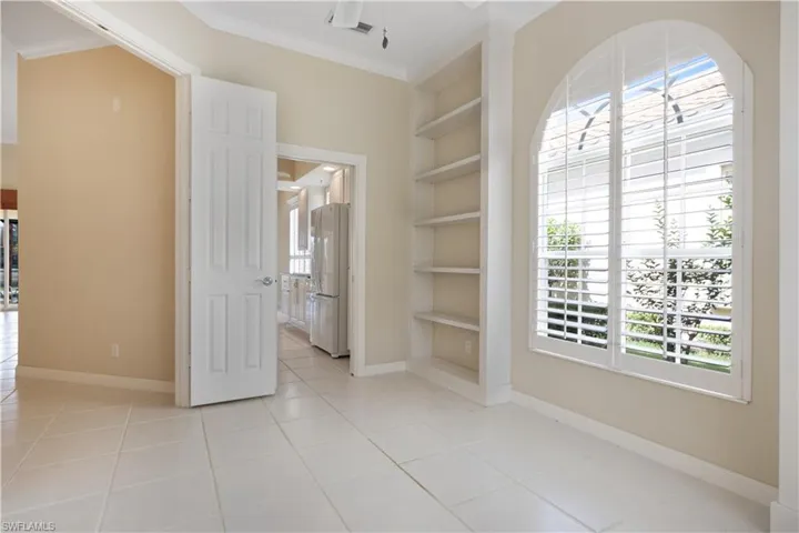 Den with built in shelves, light tile patterned floors, ceiling fan, baseboards, and crown molding and Plantation Shutters