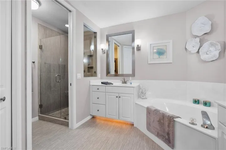 Modern bathroom featuring a glass-enclosed shower with tiled walls and a built-in niche, a white vanity with under-cabinet lighting, a rectangular mirror, and a built-in bathtub with chrome fixtures