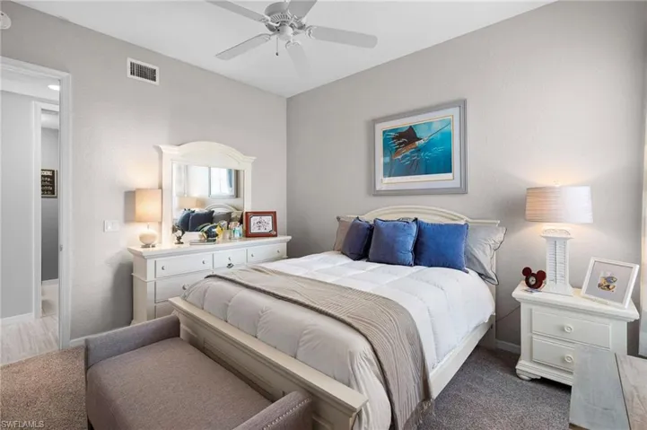 Bedroom featuring light gray wall paint, textured carpeting, a ceiling fan with integrated lighting, and a white interior door