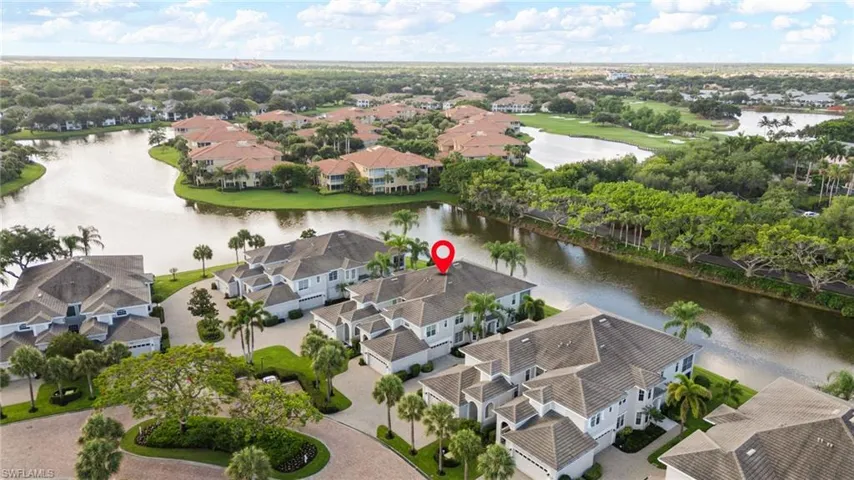 Aerial view of a residential community featuring a waterway, mature landscaping, and multiple properties with tile roofs