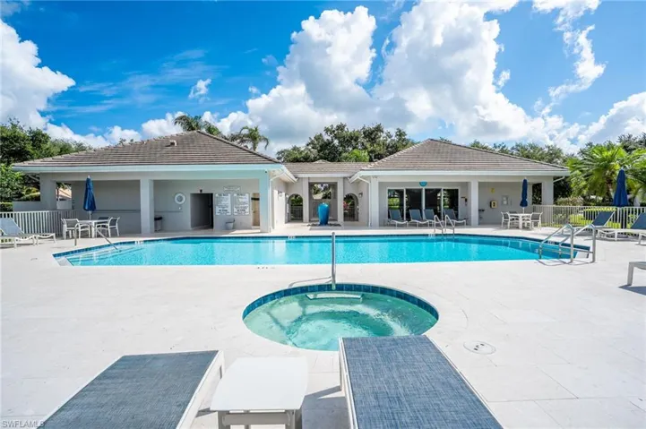 Resort-style swimming pool featuring a separate spa, expansive surrounding deck, covered outdoor seating areas, and a clubhouse with large sliding glass doors