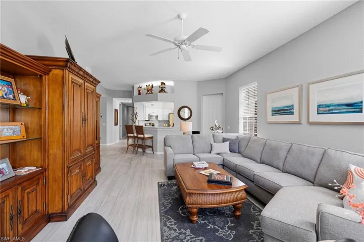 Open-concept living space with light wood-finish flooring, a ceiling fan, and a kitchen pass-through with breakfast bar seating