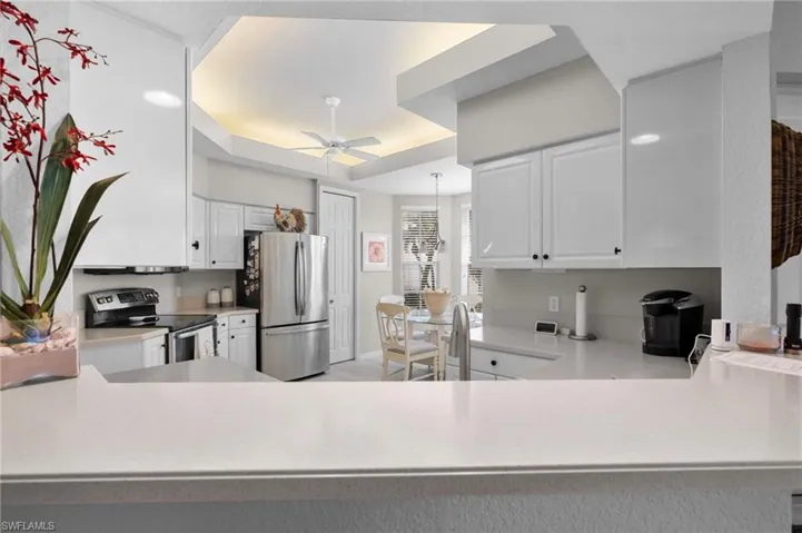 Kitchen featuring a peninsula breakfast bar with light-toned countertops, white cabinetry with black hardware, stainless steel appliances, and a tray ceiling with recessed lighting and a ceiling fan