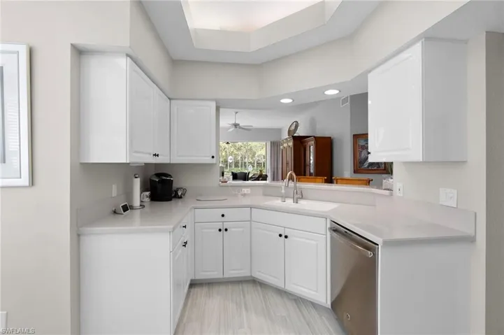 Kitchen featuring white cabinetry, light countertops, stainless-steel dishwasher, and wood-finish flooring