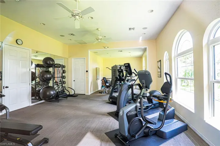 Dedicated fitness room featuring arched windows, recessed lighting, ceiling fans, and mirrored walls