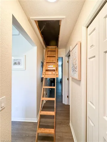 Hall with a textured wall, wood finished floors, a textured ceiling, and stairs