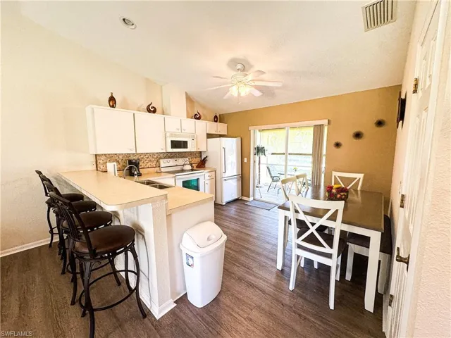 Kitchen featuring a peninsula, light countertops, lofted ceiling, a breakfast bar, and white appliances