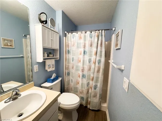 Bathroom with a textured wall, a textured ceiling, vanity, curtained shower, and dark wood-style floors
