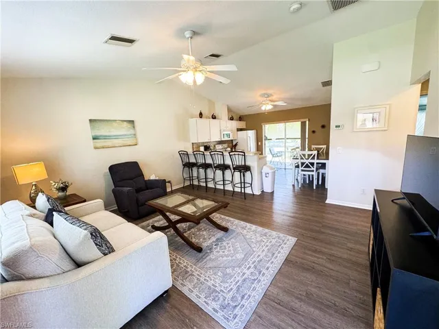 Living area with dark wood-type flooring, vaulted ceiling, and ceiling fan