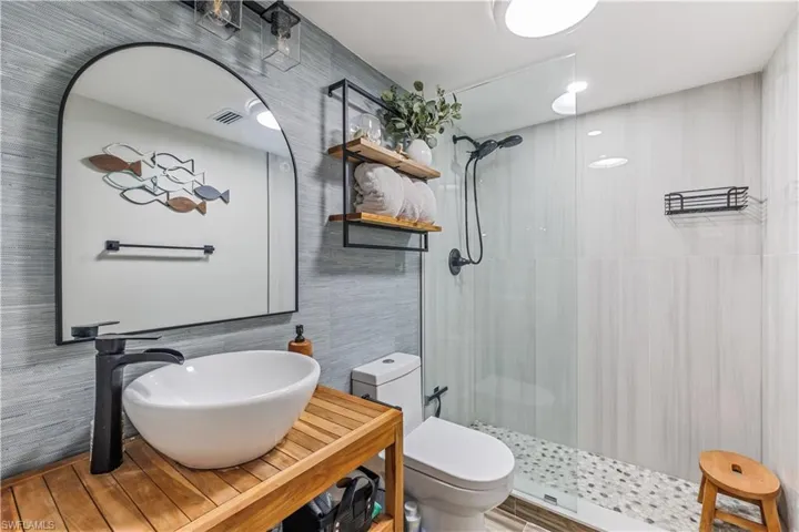 Bathroom featuring sink, tiled shower, toilet, and tile walls