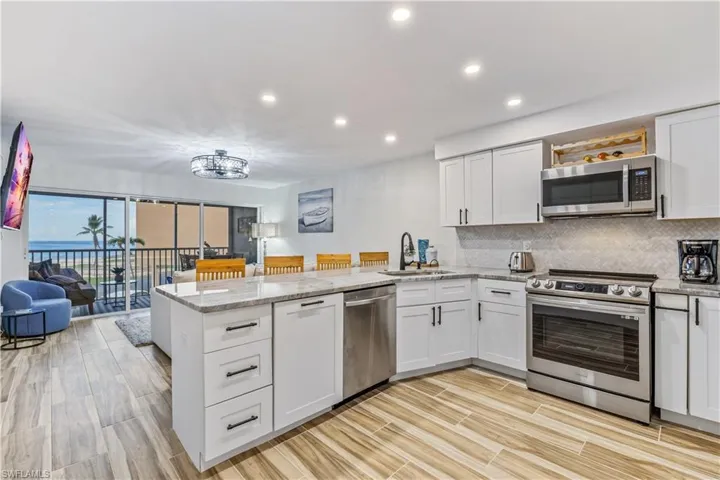 Kitchen featuring appliances with stainless steel finishes, white cabinets, kitchen peninsula, and light stone counters