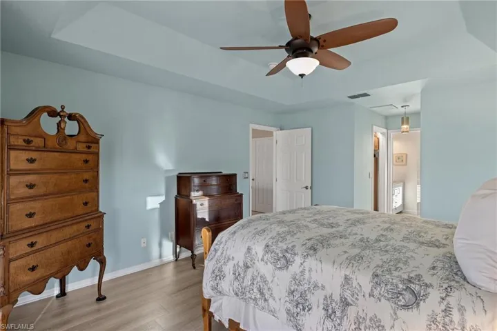 Bedroom featuring ensuite bath, a raised ceiling, ceiling fan, and light hardwood / wood-style flooring
