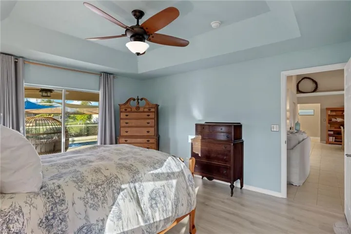 Bedroom featuring ceiling fan, access to exterior, light hardwood / wood-style flooring, and a tray ceiling