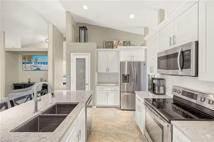 Kitchen featuring appliances with stainless steel finishes, a sink, white cabinets, decorative backsplash, and lofted ceiling