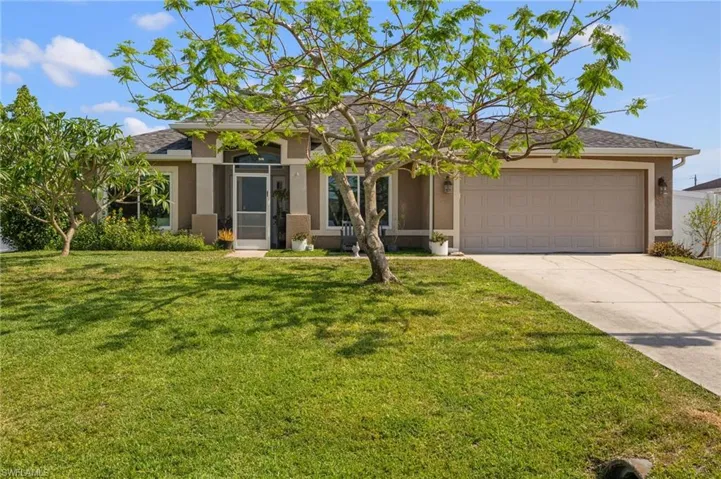 View of front facade featuring stucco siding, driveway, a front yard, and a garage