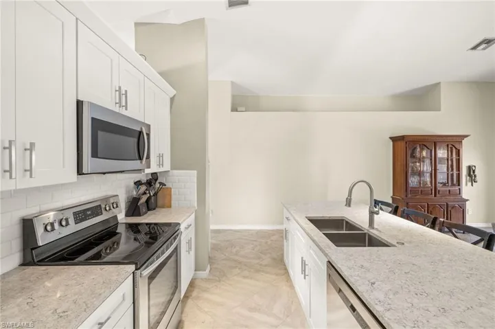 Kitchen featuring stainless steel appliances, a sink, decorative backsplash, white cabinets, and light stone countertops
