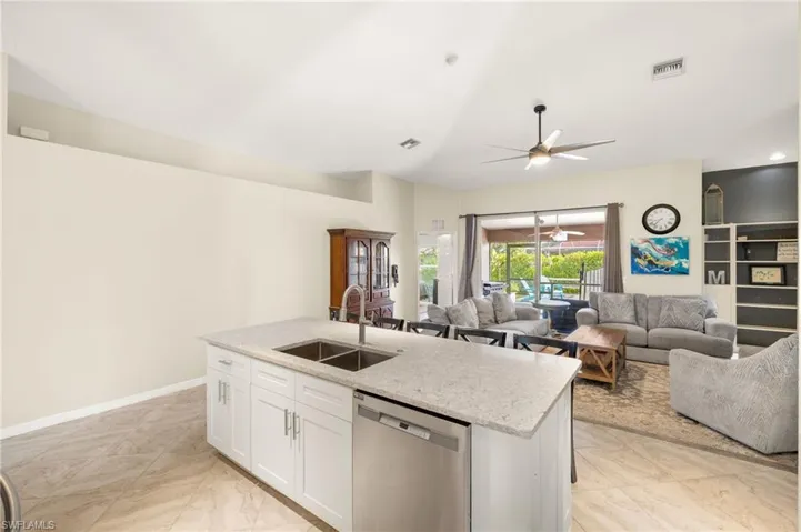 Kitchen with stainless steel dishwasher, a sink, a ceiling fan, light stone counters, and white cabinetry