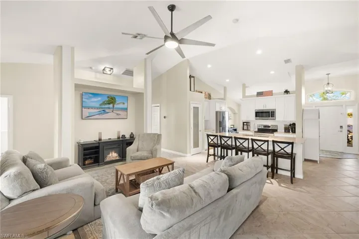 Living area with a ceiling fan, a lit fireplace, high vaulted ceiling, recessed lighting, and light tile patterned flooring