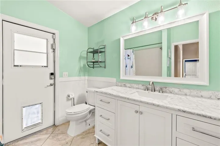 Full bathroom featuring a wainscoted wall, toilet, vanity, and curtained shower