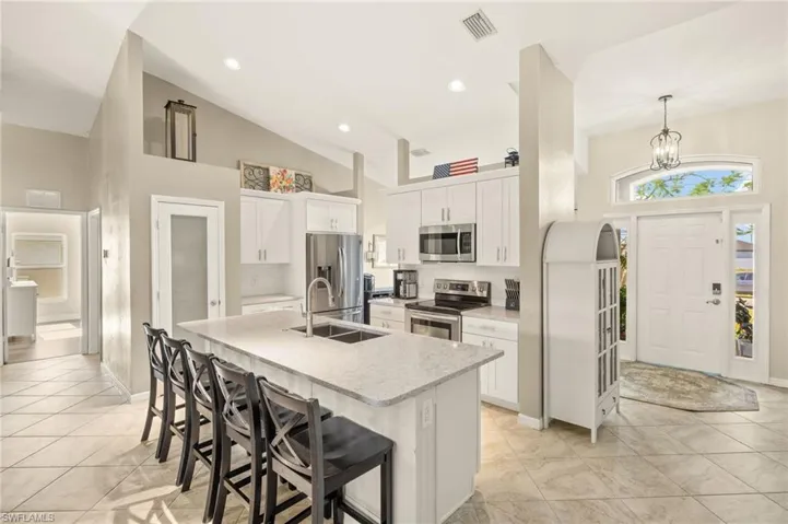 Kitchen featuring appliances with stainless steel finishes, a sink, a kitchen bar, a kitchen island with sink, and white cabinets