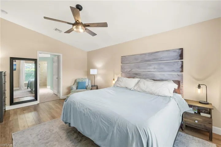 Bedroom featuring vaulted ceiling, wood-type flooring, baseboards, a ceiling fan, and ensuite bath