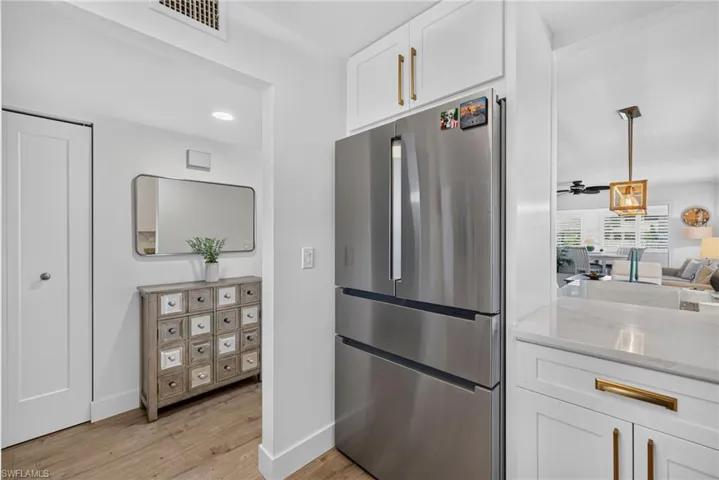 Stainless steel French-door refrigerator, white shaker-style cabinetry with gold-tone hardware, wood-finish flooring, and recessed ceiling lighting