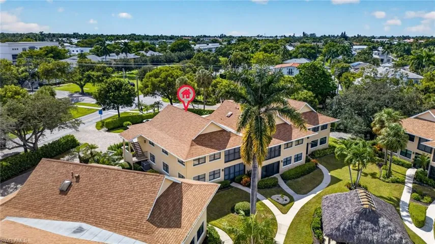 Multi-level structure featuring a pitched shingle roof, stucco exterior, screen-enclosed balconies, and mature palm landscaping