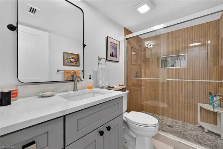 Bathroom featuring a gray vanity with a stone countertop, rectangular undermount sink, framed mirror, and a walk-in shower with floor-to-ceiling tile, sliding glass door, and integrated shower niche