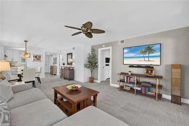 Living area featuring textured accent wallpaper, wall-mounted display, carpeted flooring, and a ceiling fan