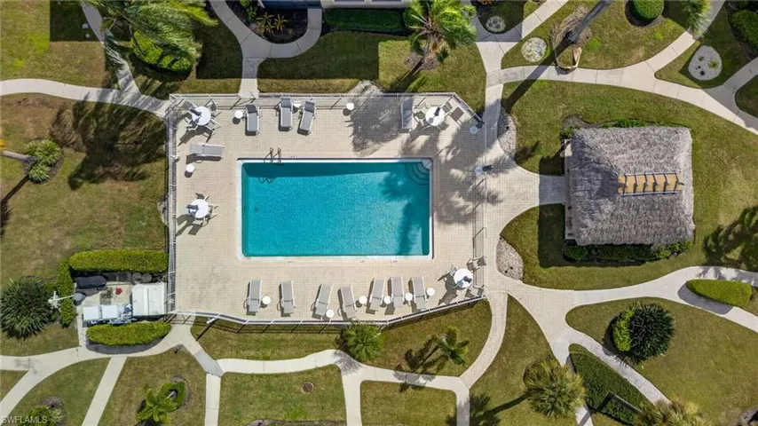 Swimming pool with surrounding paver deck, thatch-roofed cabana, manicured lawn, and interconnected concrete walkways