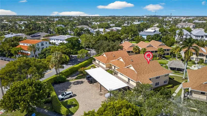 Aerial perspective of a multi-unit property featuring a shingled roof, covered parking structure, and mature landscaping
