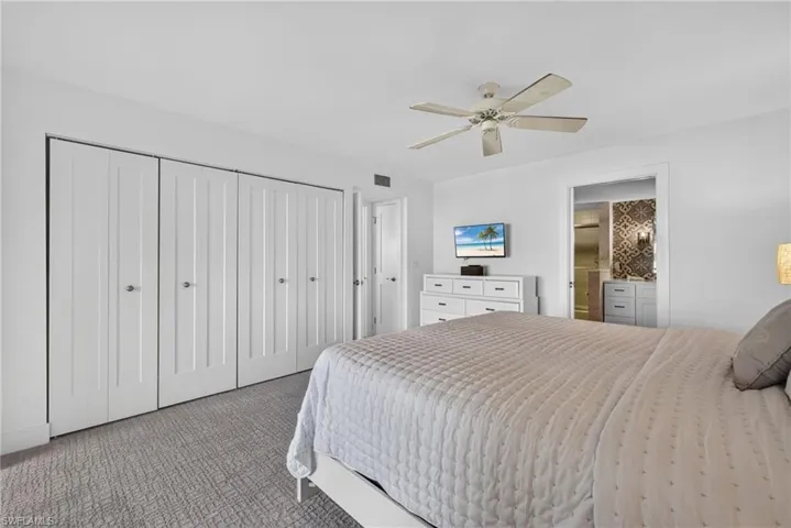 Neutral-toned carpeting, white floor-to-ceiling bi-fold closet doors, and a ceiling fan with integrated lighting