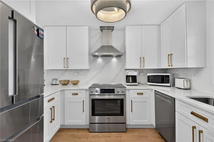 Kitchen featuring white shaker cabinetry, stainless steel appliances, stone-patterned backsplash, wood-finish flooring, and a modern circular pendant light