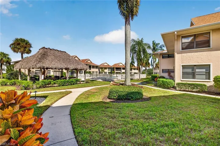 Exterior grounds featuring a thatched-roof gazebo, paved walking paths, manicured landscaping, and palm trees