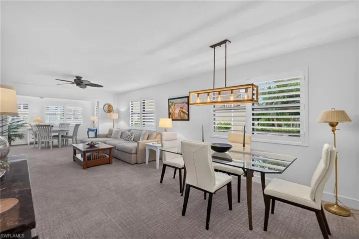 Open-concept interior featuring wall-to-wall carpeting, rectangular geometric pendant lighting, plantation shutters, and a ceiling fan