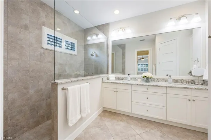 Primary bathroom has frameless glass, doorless shower enclosure, dual sinks, linen closet and multiple towel racks