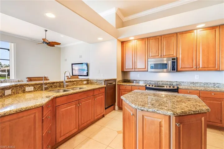 Kitchen with stainless steel appliances, a sink, ornamental molding, light stone countertops, and light tile patterned floors