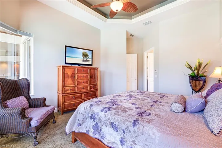 Carpeted bedroom with a raised ceiling, a ceiling fan, and crown molding