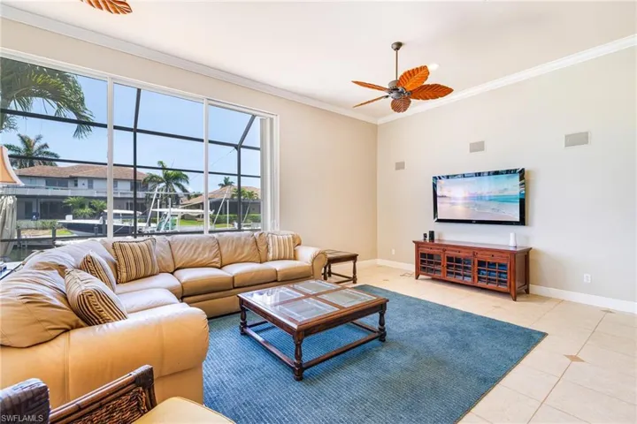 Living room with baseboards, light tile patterned flooring, ornamental molding, a ceiling fan, and plenty of natural light