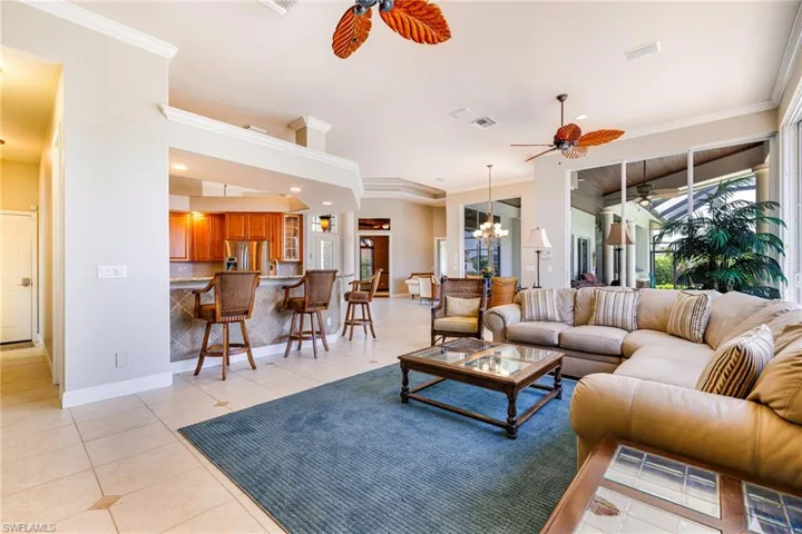 Living area with ceiling fan, light tile patterned floors, baseboards, ornamental molding, and a chandelier