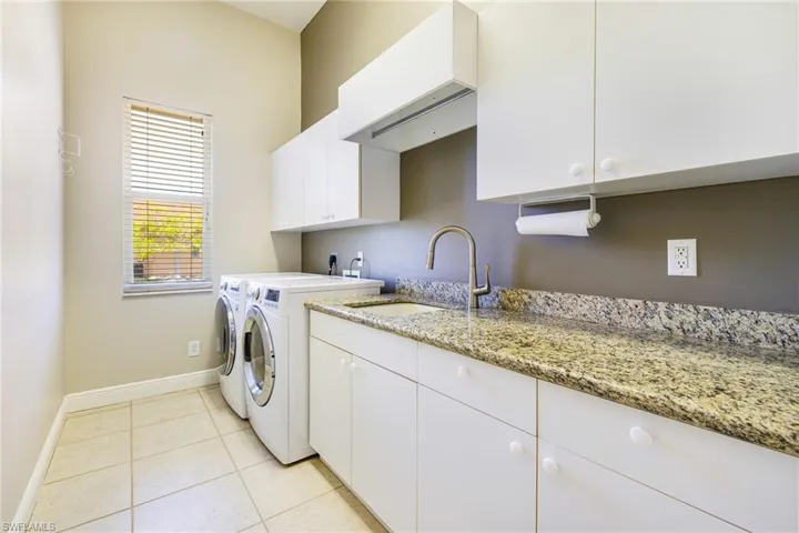 Washroom featuring washing machine and clothes dryer, cabinet space, baseboards, and light tile patterned flooring