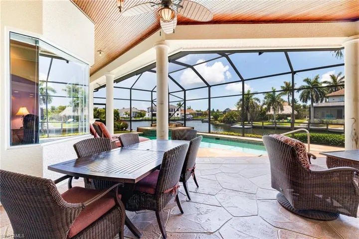 View of patio featuring a ceiling fan, an outdoor pool, a water view, and glass enclosure