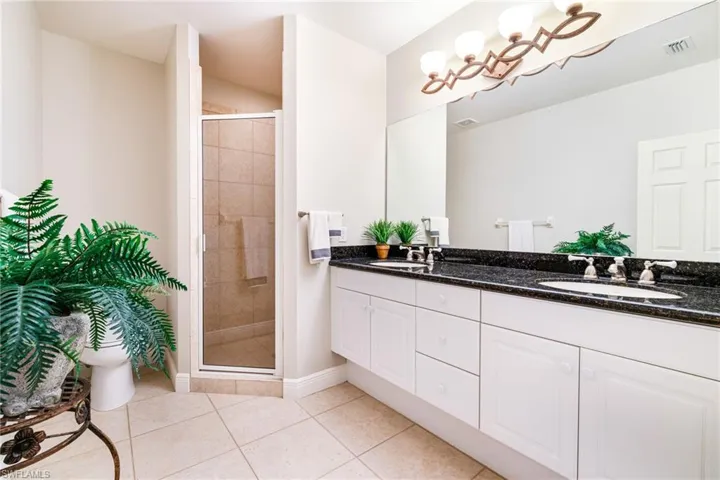 Full bathroom featuring double vanity, a shower stall, tile patterned floors, and baseboards