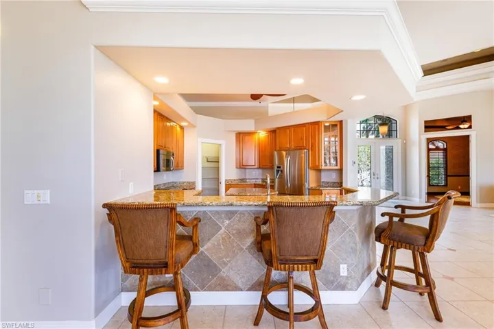Kitchen featuring appliances with stainless steel finishes, brown cabinetry, a raised ceiling, crown molding, and glass insert cabinets