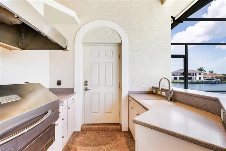 Kitchen featuring a sink, a textured wall, white cabinetry, a water view, and under cabinet range hood