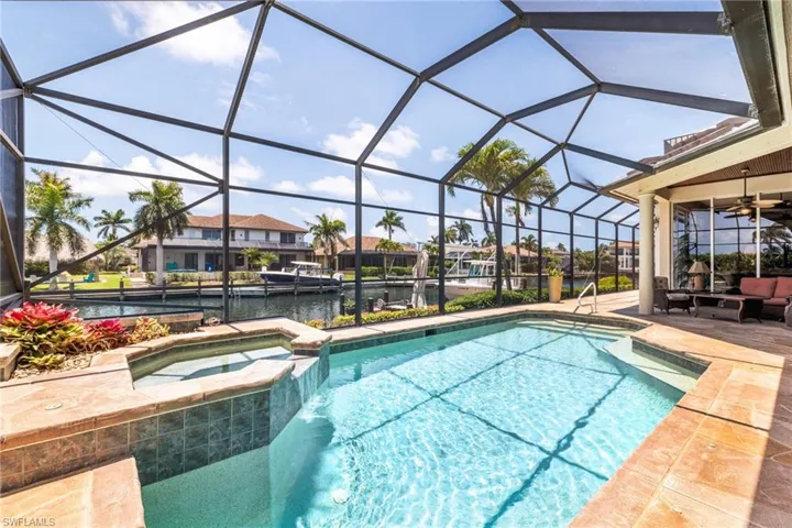 View of pool with a water view, a ceiling fan, a patio, a pool with connected hot tub, and glass enclosure